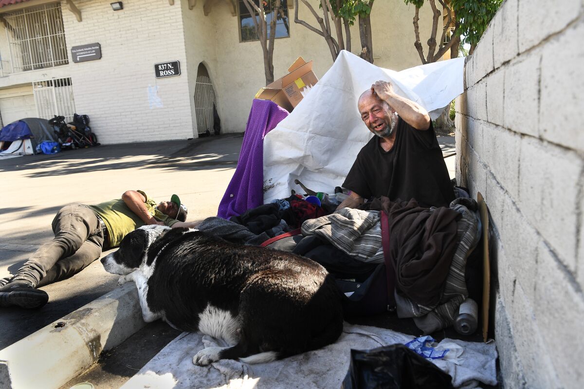 Two men and a dog at a homeless camp in a parking lot