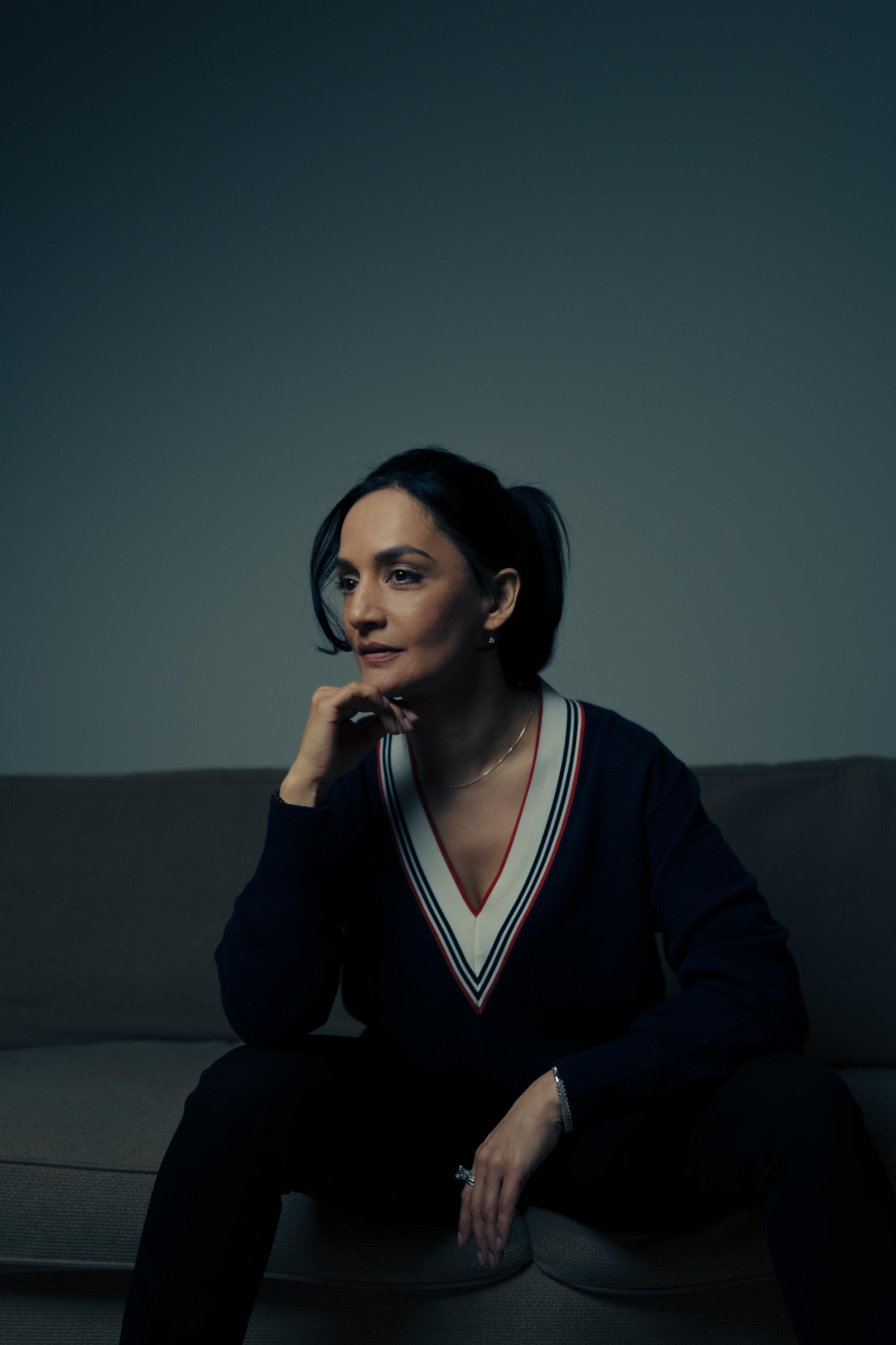 Archie Panjabi, seated, in a dark sweater with a white V-neck