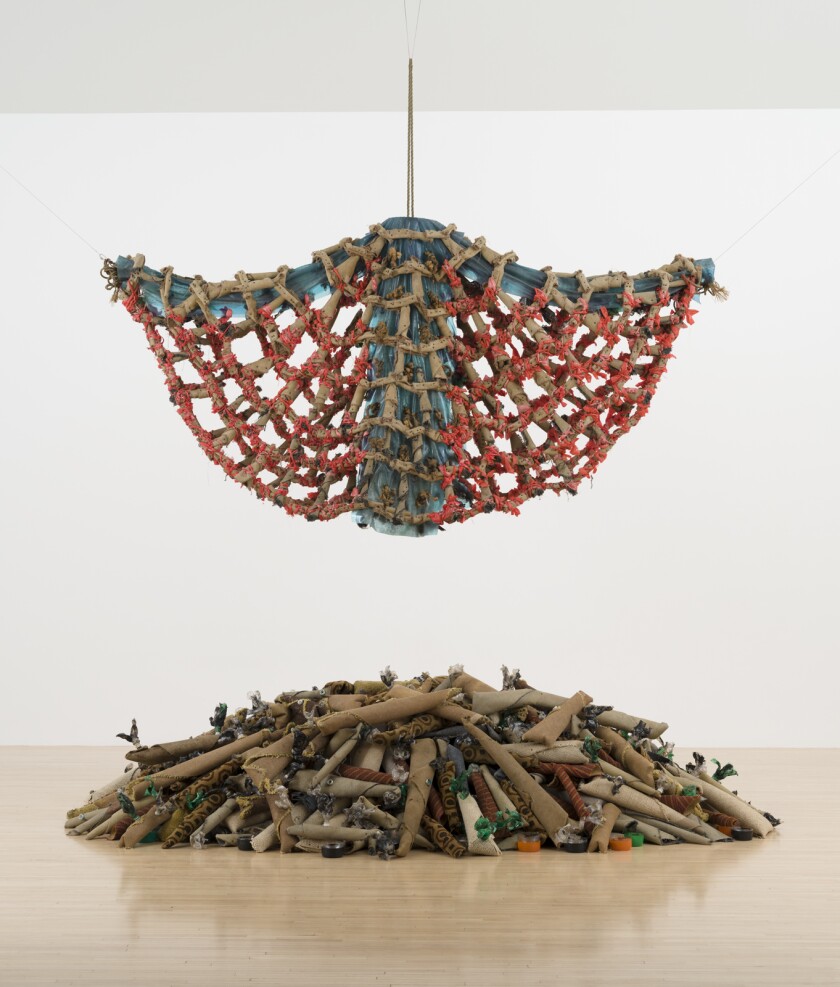 Rolled-up carpet bits are used to construct an angel shape that hovers over a gallery floor also bearing carpet rolls
