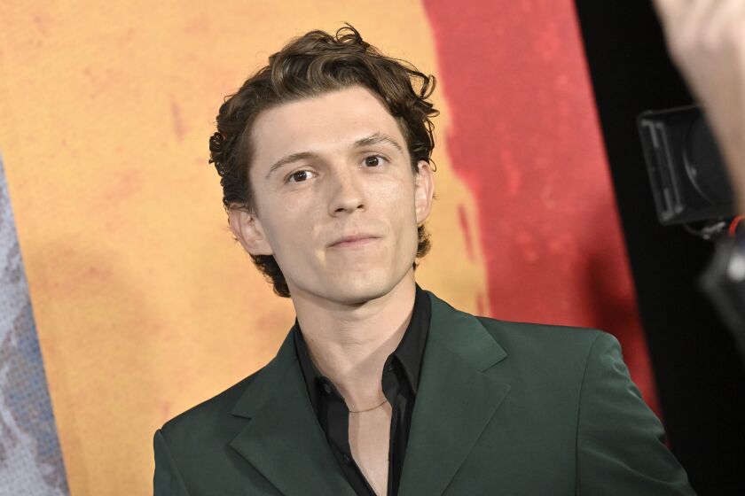 Tom Holland poses in a green suit and black collared shirt.
