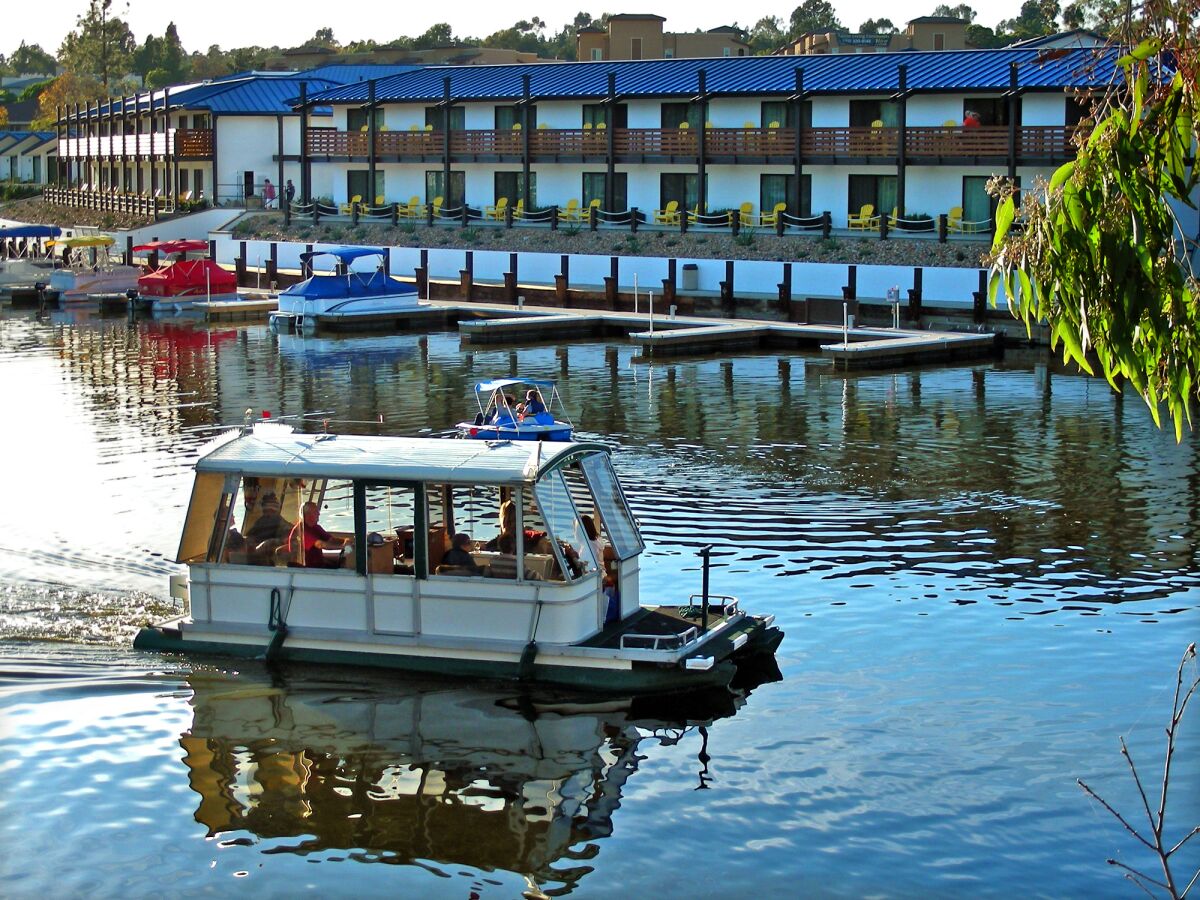 A flat bottom boats motors along on Lake San Marcos past The Lakehouse Hotel and Resort.