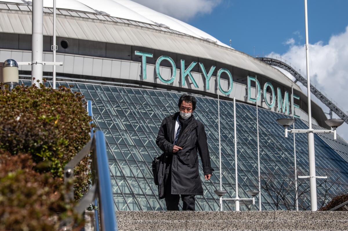 A man wearing a face mask walks past the Tokyo Dome, where baseball games will no longer be played in front of crowds because of coronavirus fears.