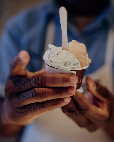 Hands hold up a paper cup with two scoops of gelato and a spoon