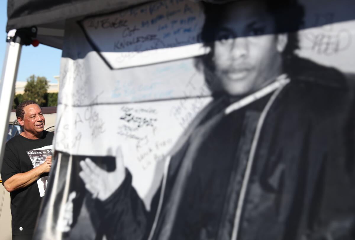 A man stands next to a banner featuring a larger-then-life-size image of rapper Eazy-E