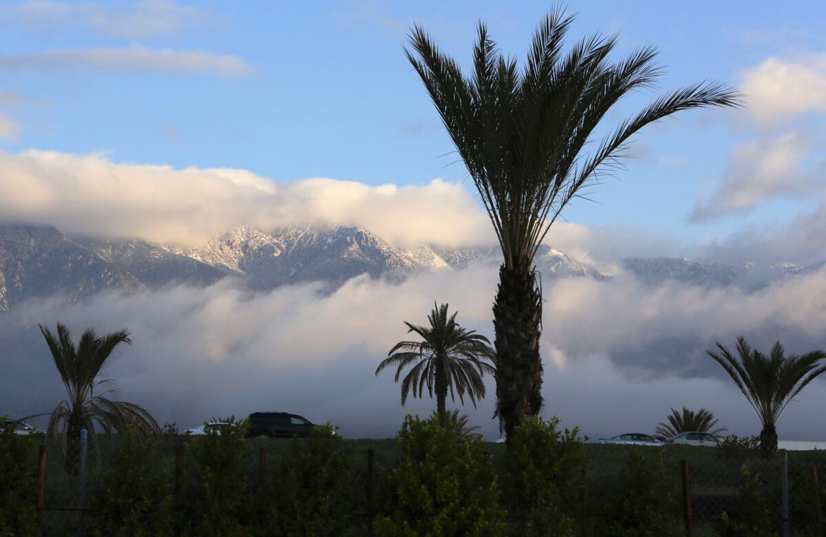 A light dusting of snow covers the San Gabriel Mountains peeking through the clouds over the Freeway 210 in Upland.