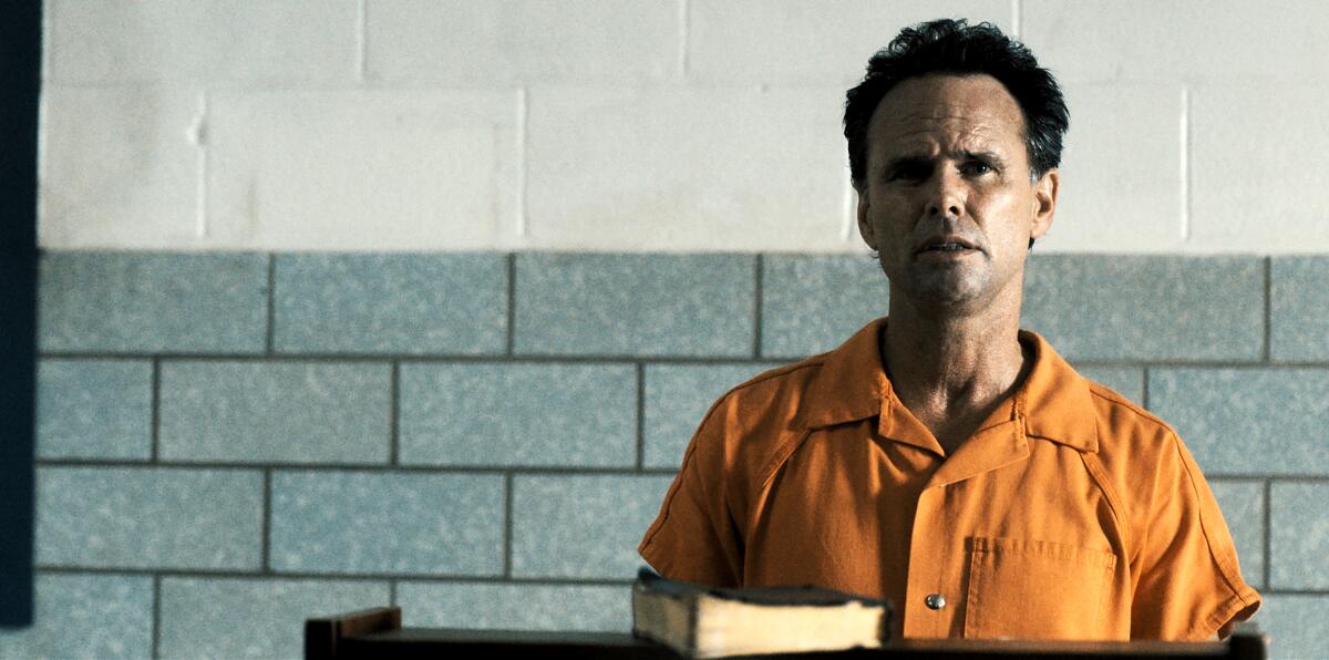 Boyd Crowder sitting in an orange jumpsuit with a book in front of him.