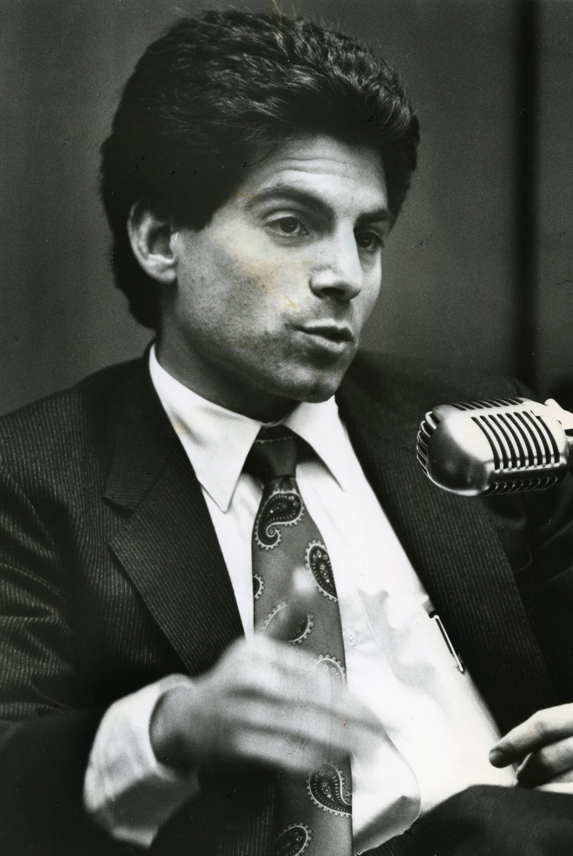 A man in a suit speaks into a microphone.