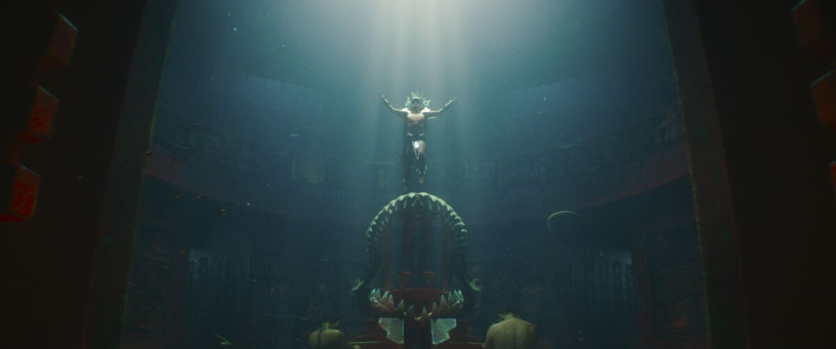 A man stands atop giant shark jaws in an underwater kingdom in a scene from "Black Panther: Wakanda Forever."