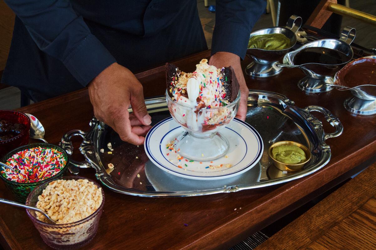 Two hands hold either side of a vanilla sundae atop a wooden bar cart at Jemma di Mare in Brentwood