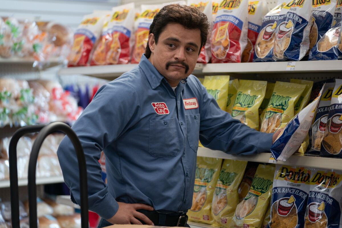 man with a mustache working in the chip aisle of a convenience store 