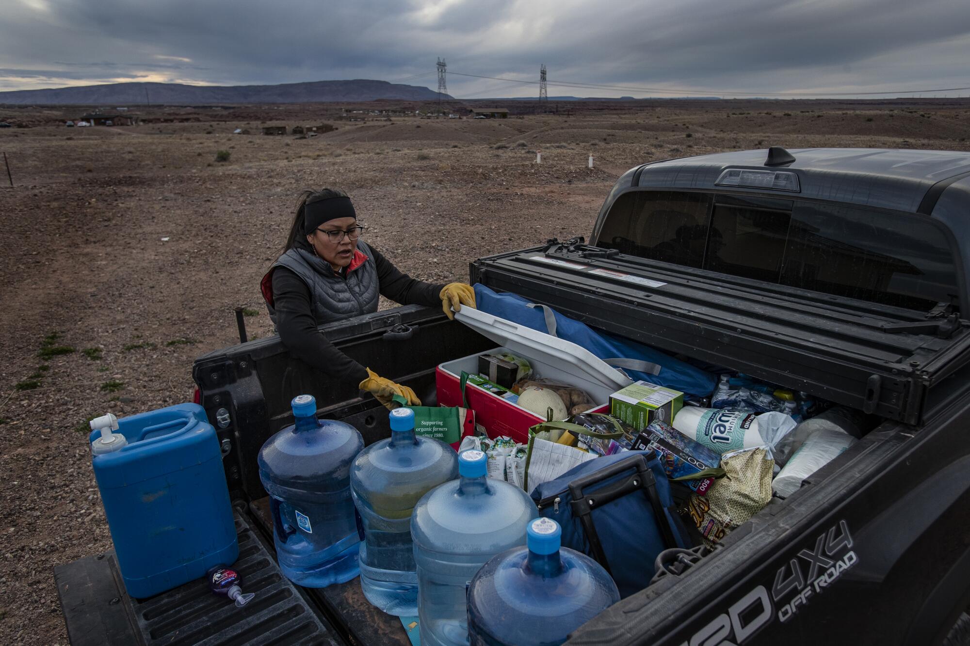 A woman unpacks jugs of water and other supplies from the bed of a pickup truck.