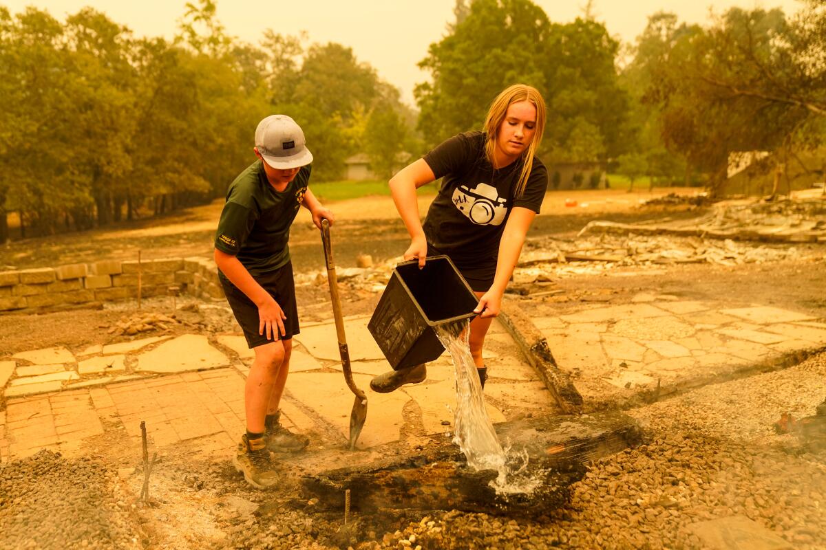 Children douse a smoldering patch of ground in water.