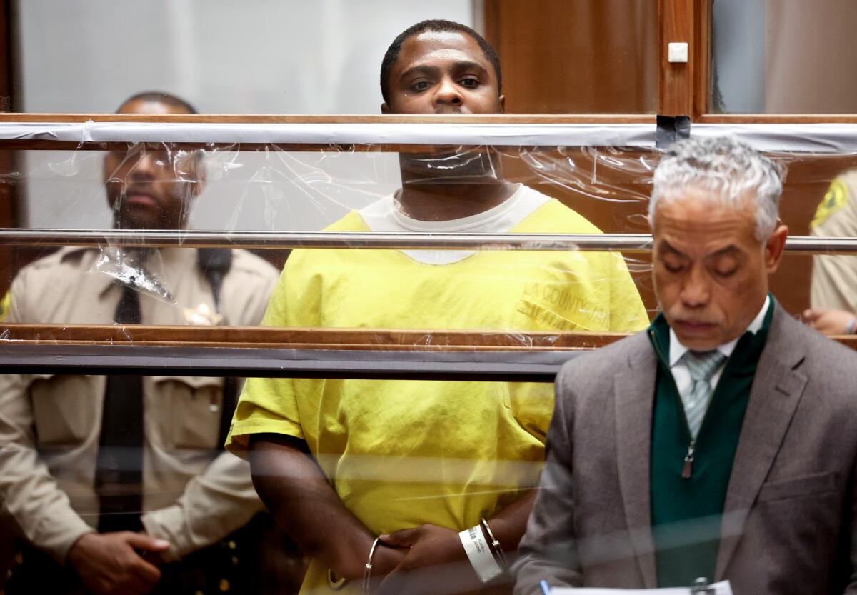 A man in yellow jail jumpsuit stands in court.