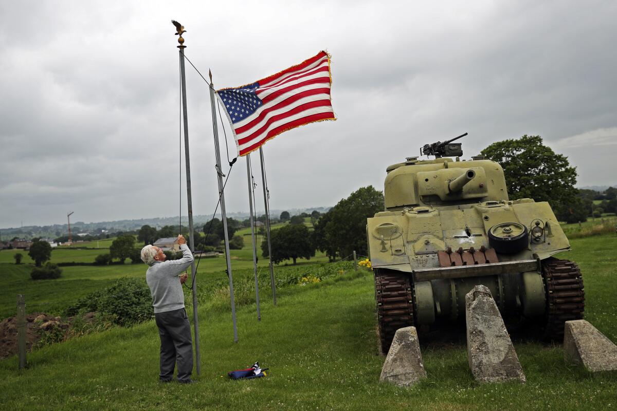 An older man raises the U.S. flag next to a tank at a Belgian museum