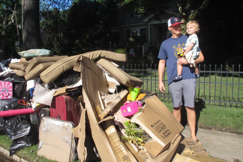 Dave Coughlin carries his 1-year-old son Thomas to their car to get him out of their flood-damaged home in Cranford N.J. on Saturday Sept. 4, 2021. His home, like many others impacted by the remnants of Tropical Storm Ida, has sewage in the basement that needs to be cleaned out. (AP Photo/Wayne Parry)