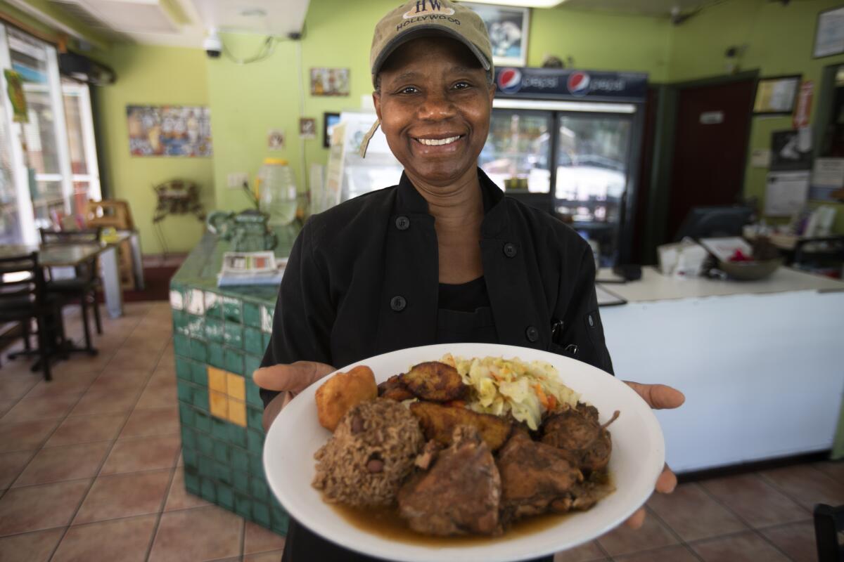 Owner Marlene Sinclair-Beckford holding jerk chicken with rice and peas, steamed vegetables, festival bread, and plantains at Ackee Bamboo.