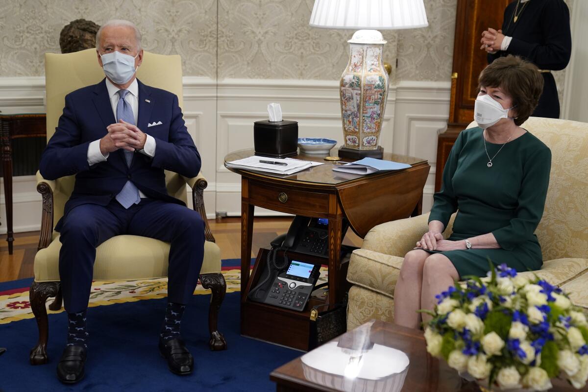 President Biden and Senator Susan Collins, wearing masks, sit on chairs in the Oval Office