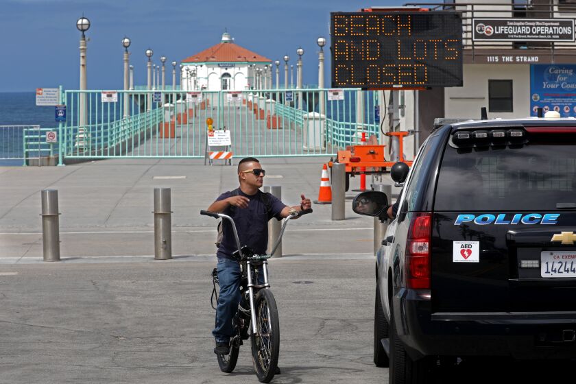 MANHATTAN BEACH, CA - JULY 03: Manhattan Beach police lets Michael Aranda know the bike path will be closed thru the weekend on Friday, July 3, 2020 in Manhattan Beach, CA. Los Angeles County Closes Beaches, Piers, Beach Parking Lots, Beach Bike Paths, and Beach Access Points for the Fourth of July Weekend due to Increased COVID-19 Cases. Closed from Friday, July 3rd at 12:00 A.M. thru Monday, July 6th at 5:00 A.M. (Gary Coronado / Los Angeles Times)