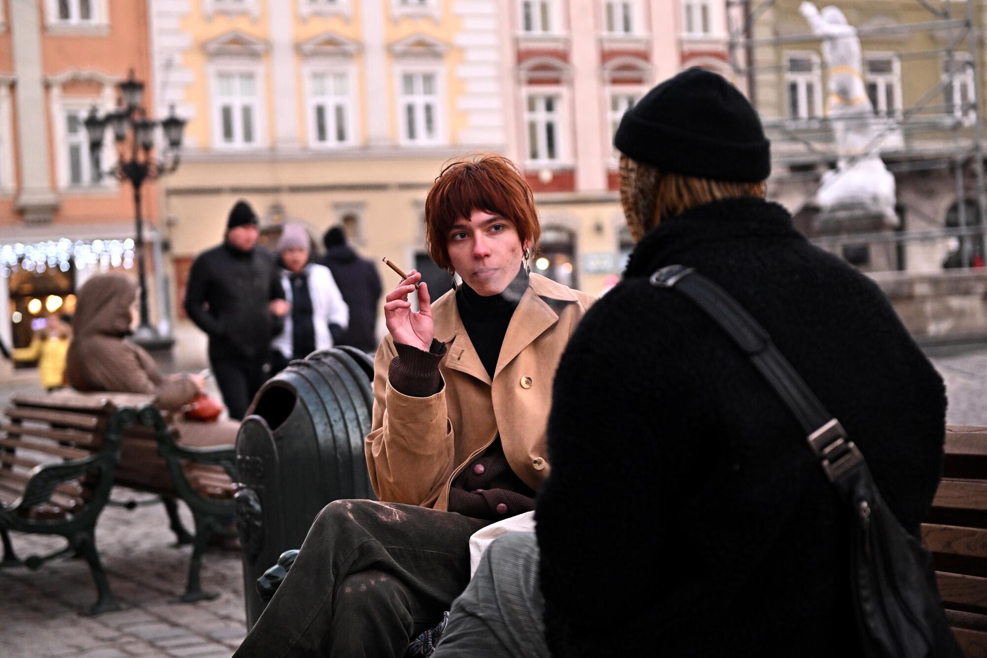 A woman holding a cigarette faces a second person on a bench  