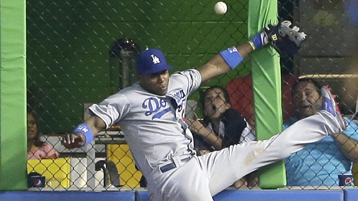 Dodgers right fielder Yasiel Puig collides with the fence while chasing after a hit by Miami's Jeff Baker during the ninth inning of the Dodgers' 5-4 loss Sunday.