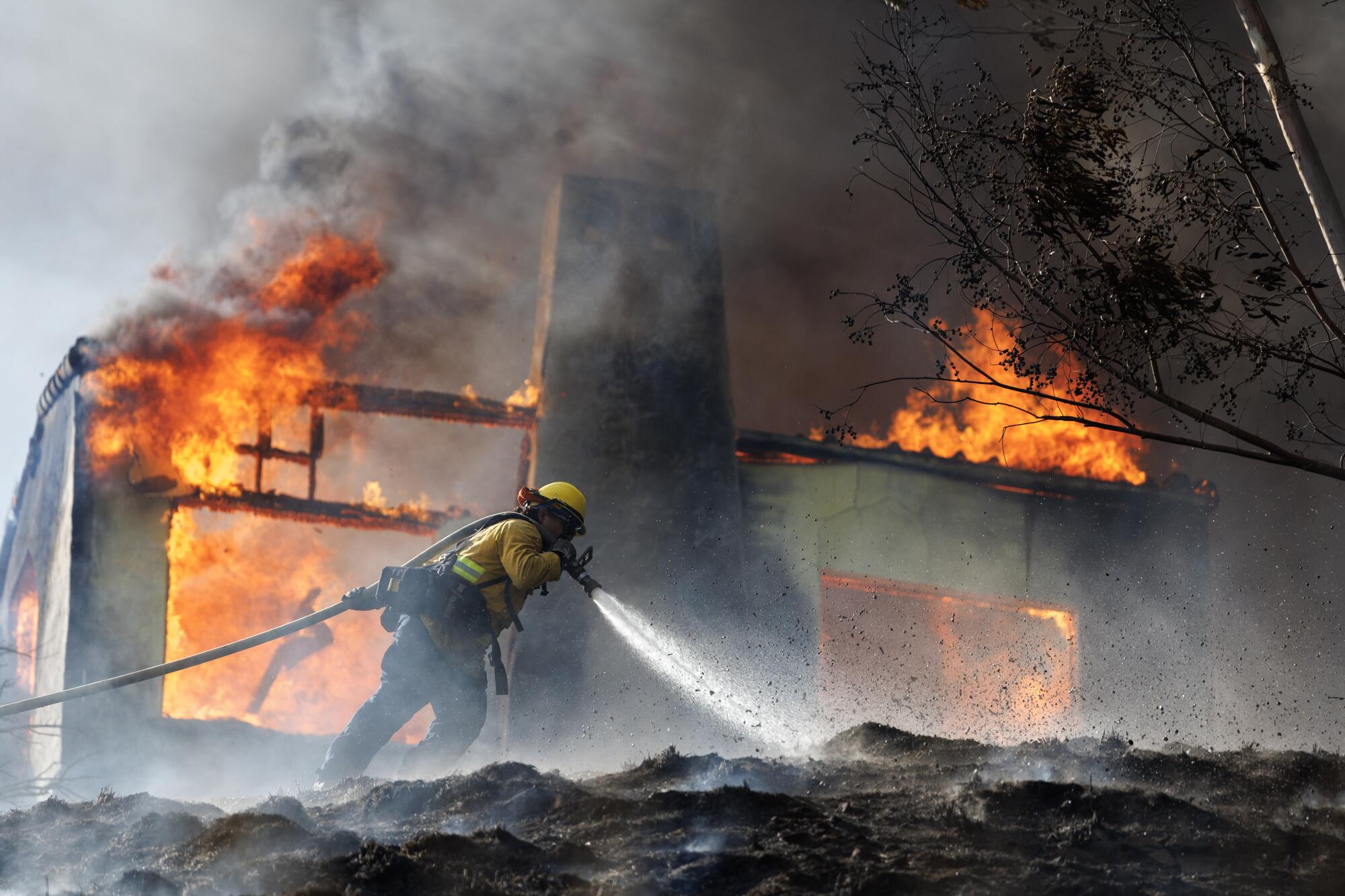 A firefighter hoses down the ground in front of burning home.