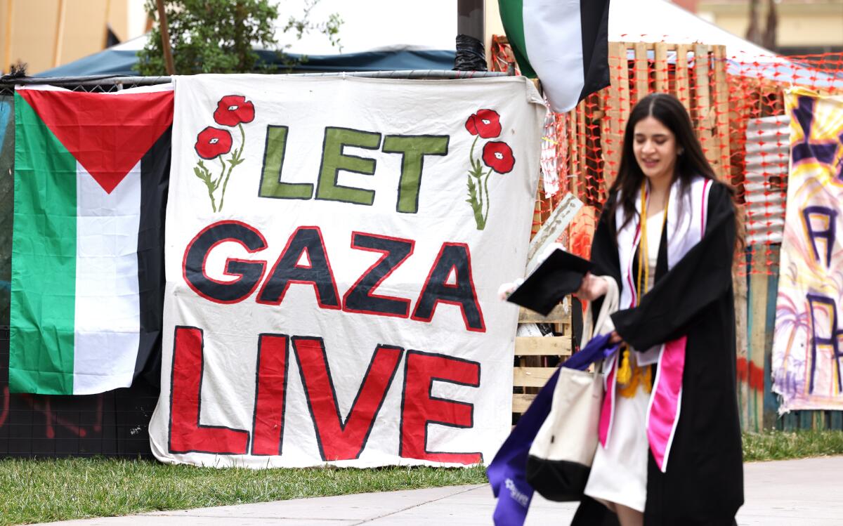 A student wearing a graduation gown passes a banner that says, "Let Gaza Live." 
