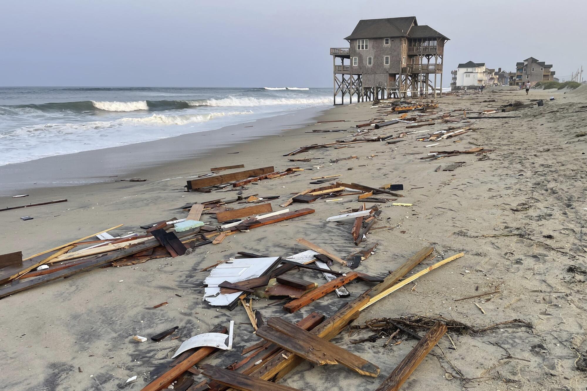 Wood debris litters a beach alongside oceanfront homes.