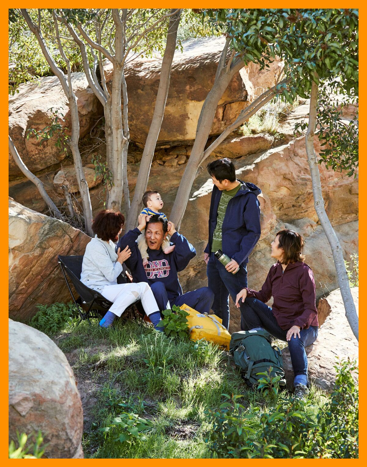 A family rests outdoors among trees and rocks.
