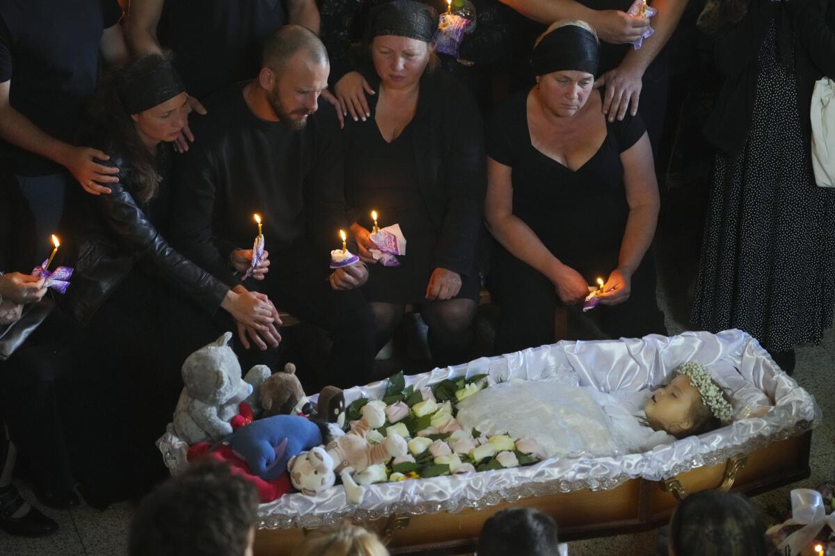 Relatives and friends sit with candles near a girl in a casket during a mourning ceremony.