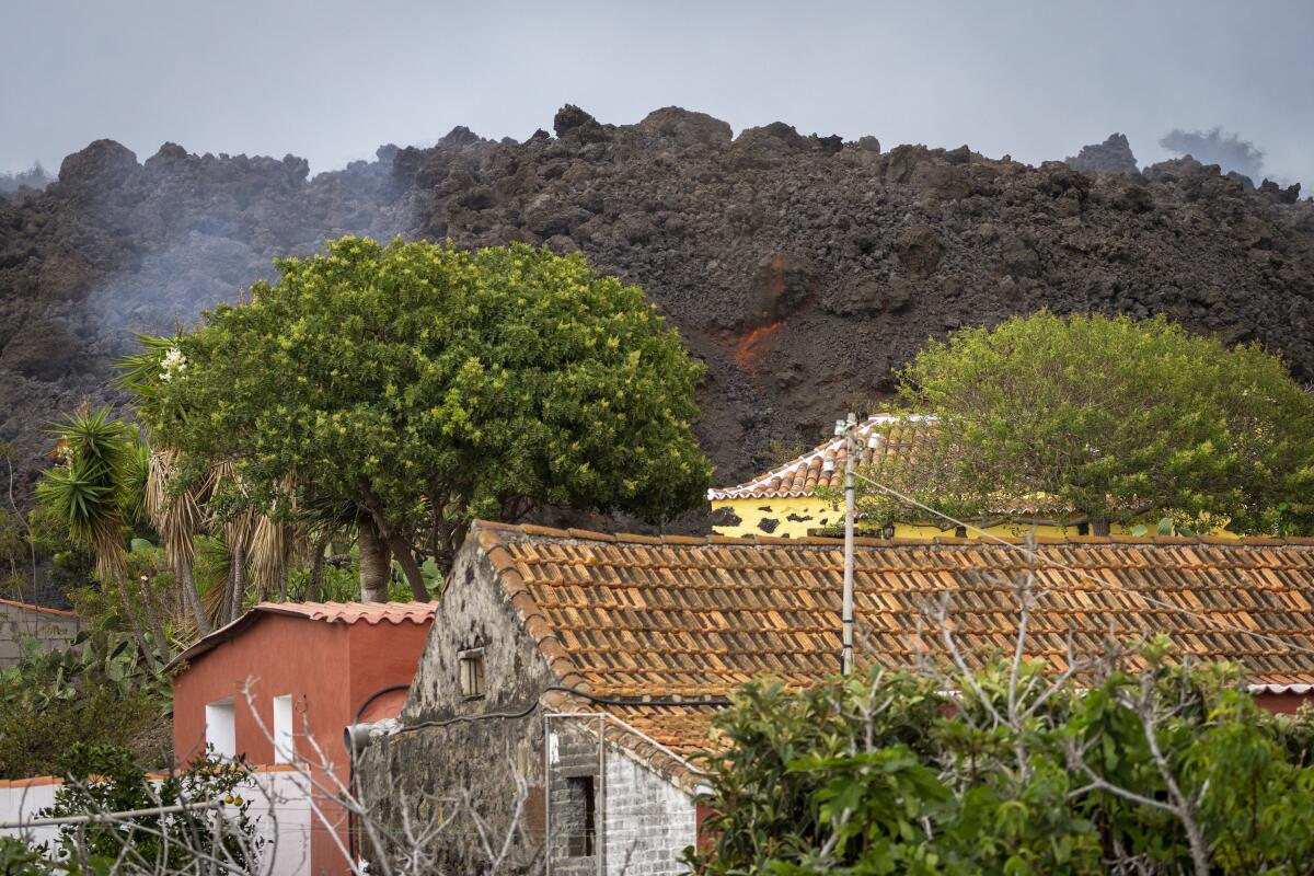 Lava flows down a hill behind houses.