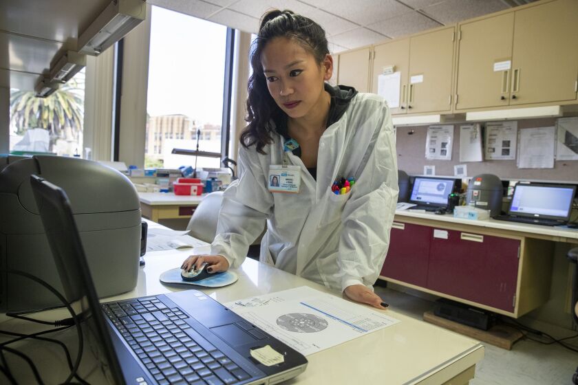 BRENTWOOD, CALIF. -- SATURDAY, MARCH 28, 2020: Clinical lab scientist Mikkiel Cheng checks the time left on a thermal cycler processing a test for Covid-19 at the UCLA clinical microbiology lab in Brentwood, Calif., on March 28, 2020. (Brian van der Brug / Los Angeles Times)