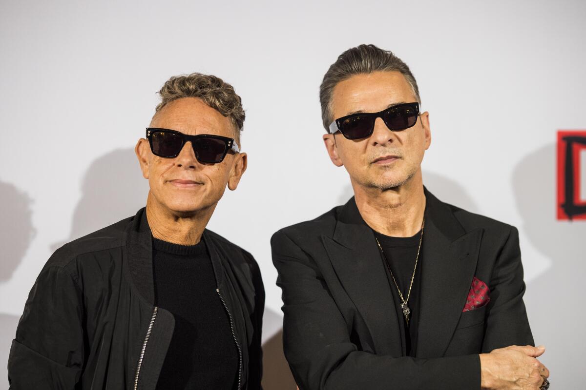 Two men wearing dark glasses and black jackets stand beside each other
