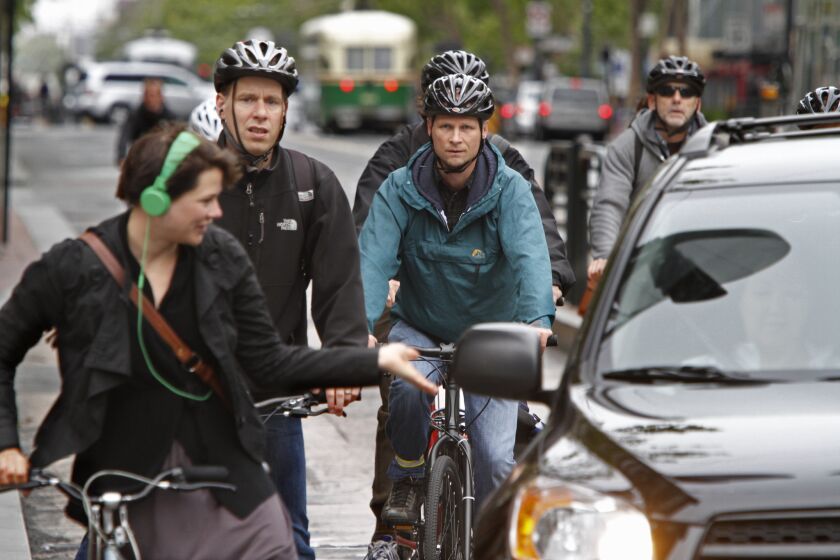 A bicyclist gestures towards a car trying to make a turn through a group during the busy morning commute along Market Street in San Francisco.