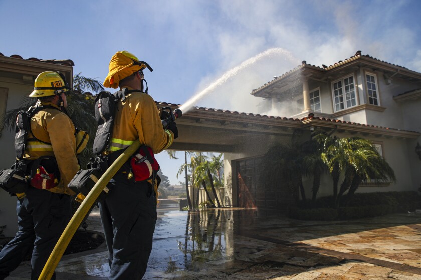 El Segundo firefighters Mathew Goodenough, left, and Javier Olmeda hose down a smoldering home in Laguna Niguel on Thursday.