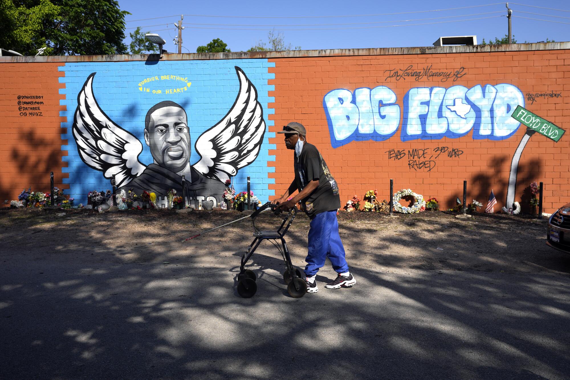 A man with a walker passes a mural bearing the image of George Floyd depicted as an angel and the words Big Floyd
