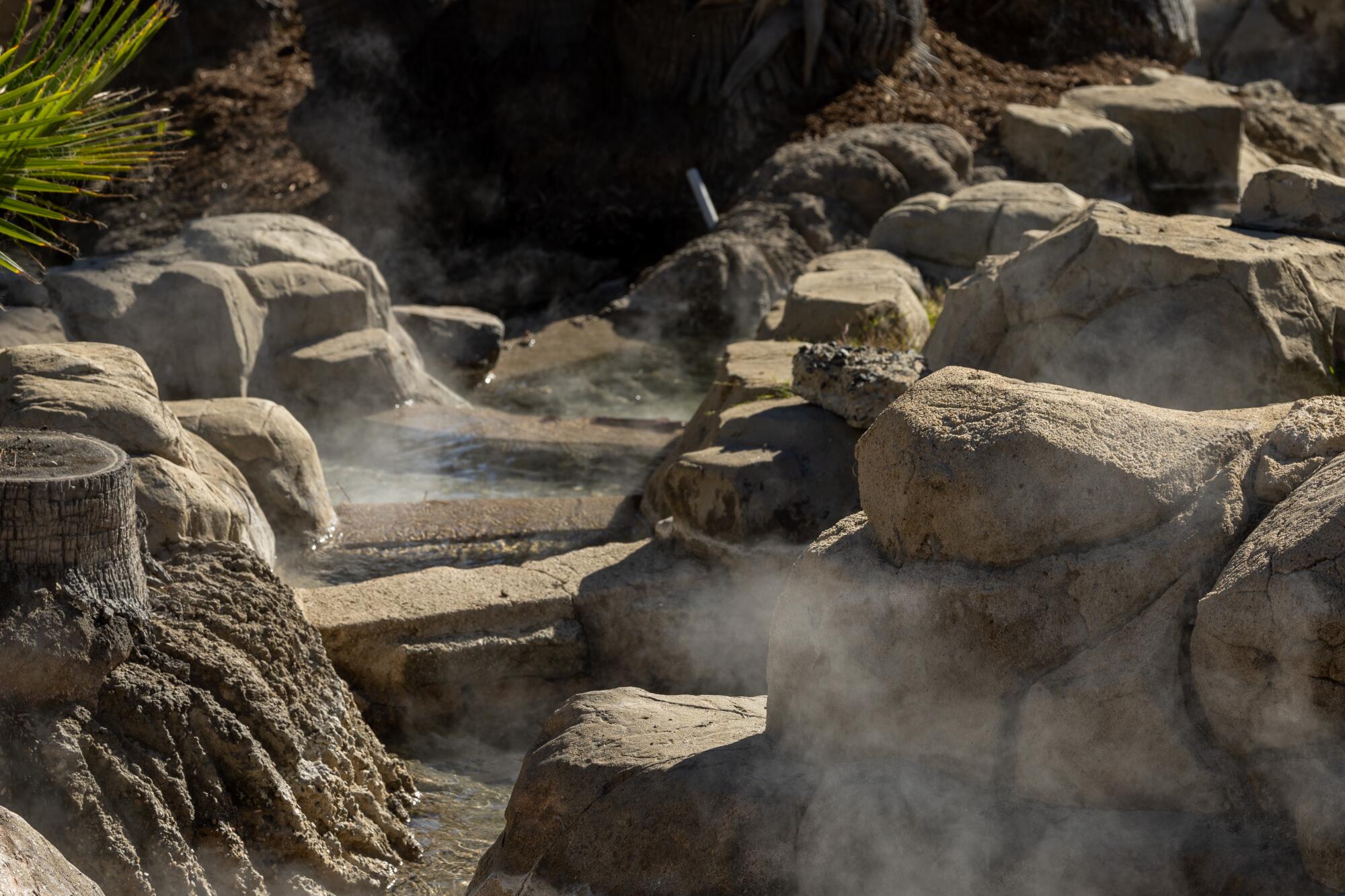 Steam rises from the geothermal water flowing among large boulders