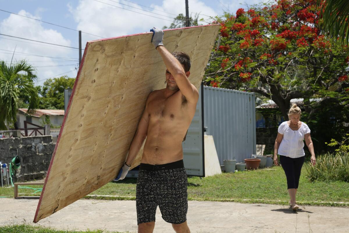 Un vecino carga un tablón de madera para cubrir las ventanas de su casa