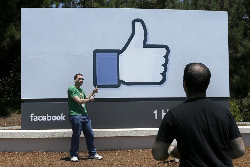 Man poses in front of the Facebook sign on the Facebook campus in Menlo Park, Calif.