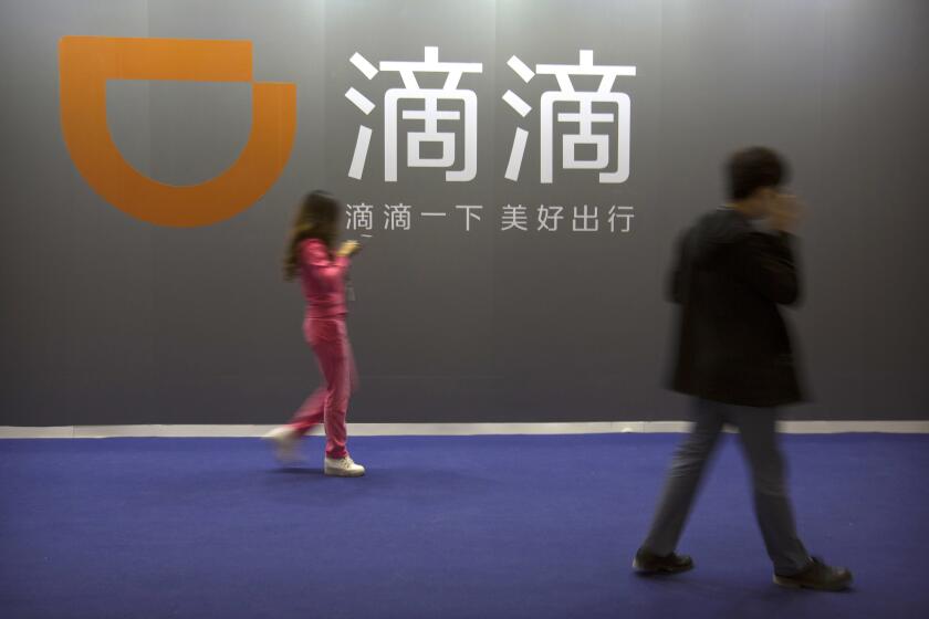 FILE - In this April 27, 2017, file photo, visitors walk past a sign for Chinese ride-hailing service Didi Chuxing at the Global Mobile Internet Conference (GMIC) in Beijing. Chinese ride-hailing service Didi says it lost $5.5 billion over the past three years ahead of its U.S. stock market debut Wednesday, June 30, 2021, but it's highlighting its global reach and investments in developing electric and self-driving cars. (AP Photo/Mark Schiefelbein,File)