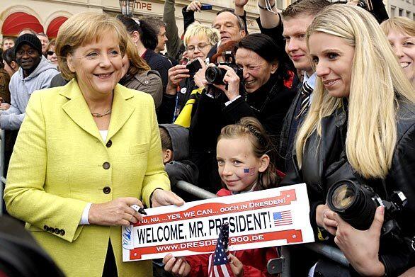 German Chancellor Angela Merkel autographs a sign held by a young girl welcoming President Obama to the eastern German city of Dresden, which was rebuilt after being repeatedly bombed by the Allies in World War II.
