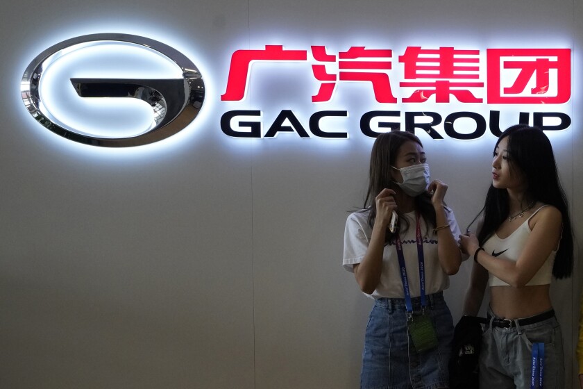 Two women stand near the logo for the Guangzhou Automobile Group Co. Ltd during an auto show in Beijing on Sunday, Sept. 27, 2020. Carmaker Stellantis moves to consolidate its position in fast-growing China looked off to a rocky start after one of its JV partners said it hadn’t been consulted before an announcement of plans to take a controlling stake. Stellantis plans to lay out its strategy March 1, but has offered some hints in announcements this week. They include plans to increase the stake in Chinese partner GAC Stellantis from 50% to 75% under new rules allowing more foreign investment, and an announcement Friday that the other JV, with Dongfeng, had doubled sales in 2021. (AP Photo/Ng Han Guan)