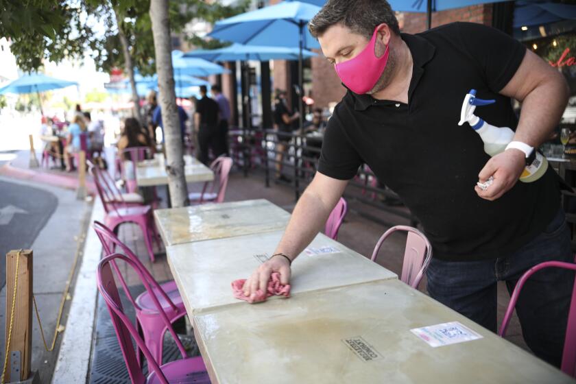 Waiter Zach Werne cleans a table at Breakfast Company in the Gaslamp Quarter in downtown San Diego on Thursday, July 16 2020.(Photo by Sandy Huffaker for The San Diego Union-Tribune)