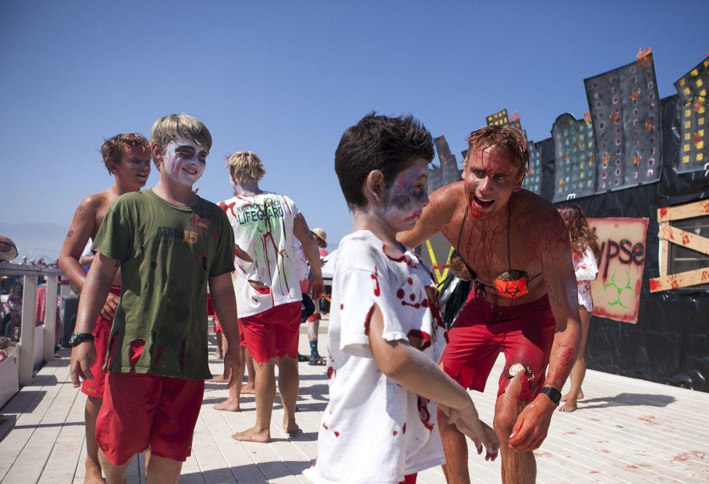 Alex Nathan, second from right, is greeted by a zombified junior lifeguard Thursday during the Newport Beach Junior Lifeguard Program’s annual Monster Mile near the Balboa Pier.