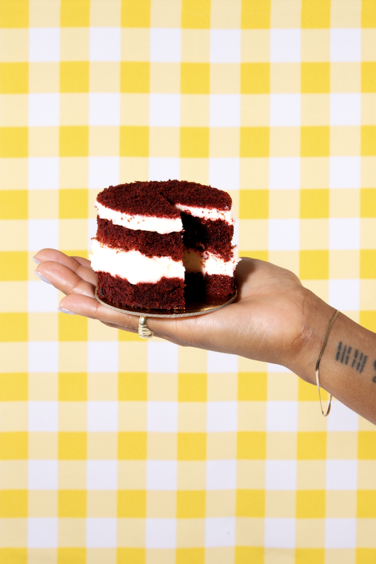A small round red velvet cake, with a slice missing, in the palm of an upraised hand