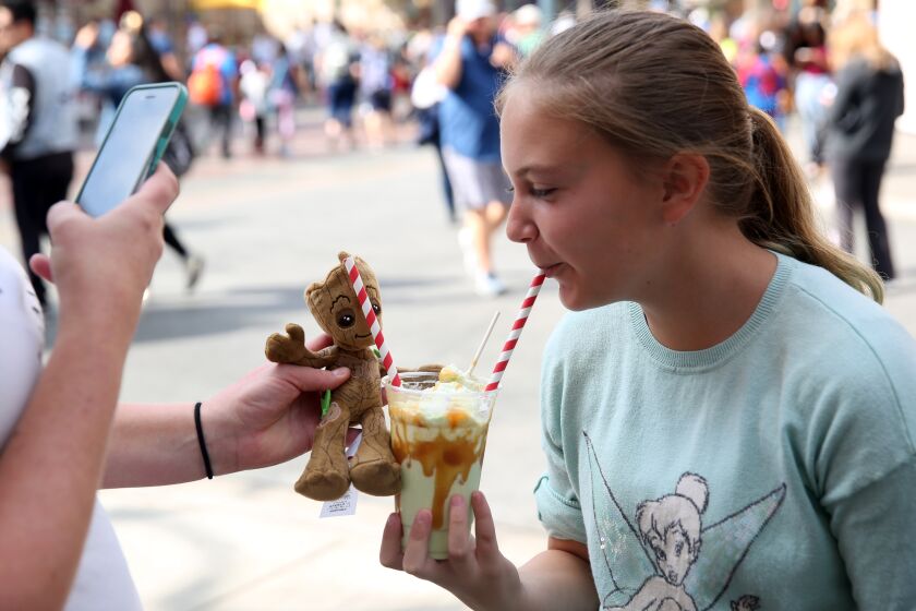 ANAHEIM, CA-OCTOBER 9, 2019: Millie Kattenhorn, left, takes a picture of daughter Katie Kattenhorn, 10, eating a Carmel Apple Smoothie to post to social media at Disney California Adventure Park on October 9, 2019 in Anaheim, California. Disneyland, and other theme parks, are creating visually interesting Halloween inspired foods with the idea that park goers might want to post them to social media. (Photo By Dania Maxwell / Los Angeles Times)
