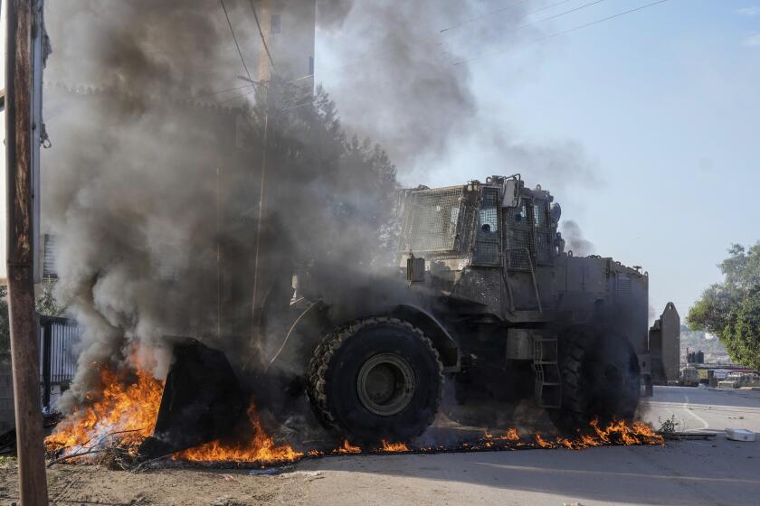 Un vehículo militar israelí retira neumáticos en llamas que bloquean una carretera durante una incursión del ejército en el campo de refugiados de Faraa, en Cisjordania, el 8 de diciembre de 2023. (AP Foto/Majdi Mohammed)