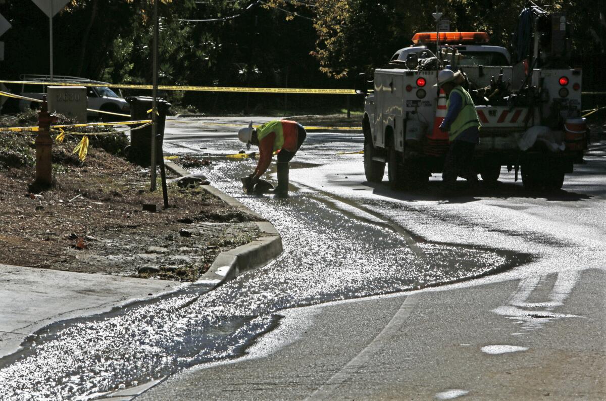 DWP worker Mike Correa places a sandbag to guide the water from a broken 12-inch water main that closed Benedict Canyon Drive in Beverly Hills on Tuesday.