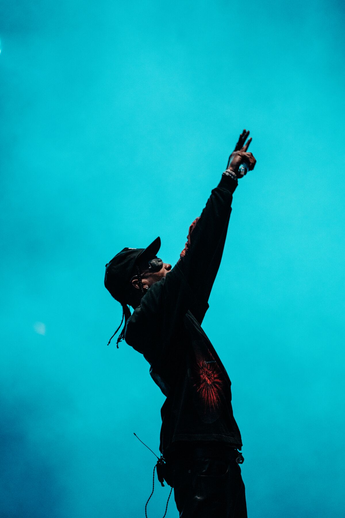 A pointing man is silhouetted against a smoky, blue stage during a concert.