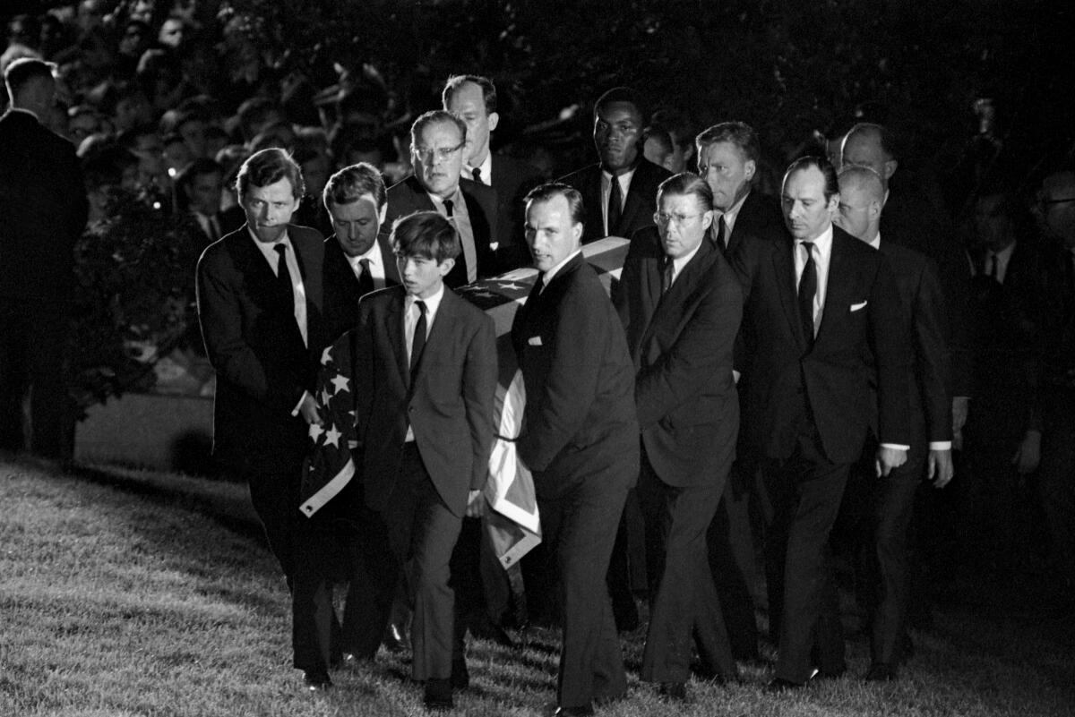 Men and one boy, wearing suits, carry a flag-draped coffin.