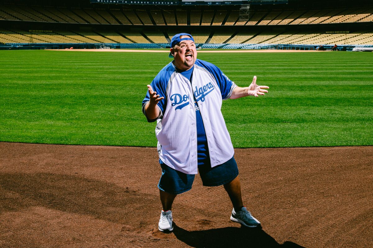 A man poses in Dodgers gear on a sunny day on the field at Dodger Stadium